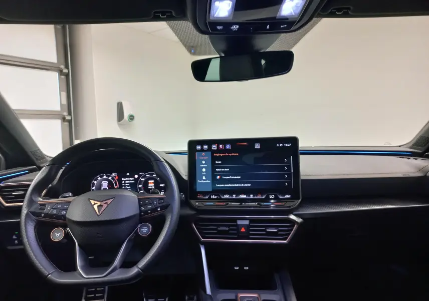 Vue intérieure du tableau de bord et volant CUPRA Leon Phase 2 avec écran tactile central et éclairage d'ambiance bleu.