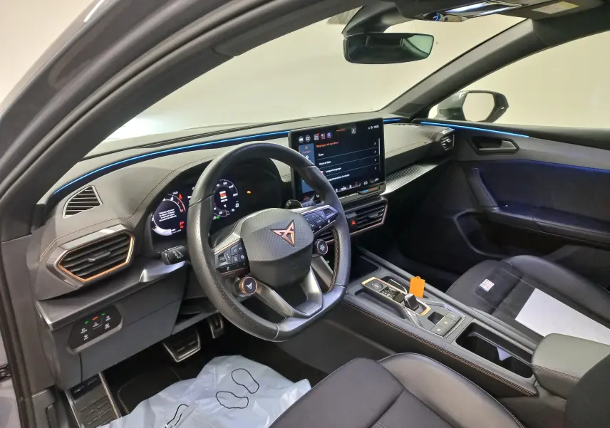 Vue intérieure côté conducteur de la CUPRA Leon Phase 2 avec éclairage d'ambiance bleu et tableau de bord numérique.
