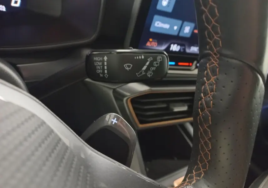 Gros plan sur la commande d’essuie-glace et le volant en cuir noir avec surpiqûres orange d’une CUPRA Leon Phase 2.