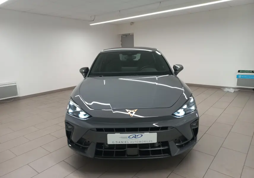 Vue avant d'une CUPRA Leon Phase 2 gris Graphene avec phares allumés et logo CUPRA lumineux au centre du capot.
