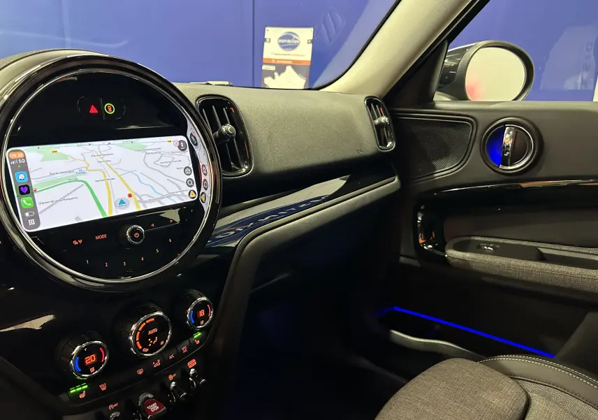 Vue intérieure côté passager du tableau de bord et console centrale d'une MINI Countryman 136 BVA avec écran tactile et éclairage d'ambiance bleu.