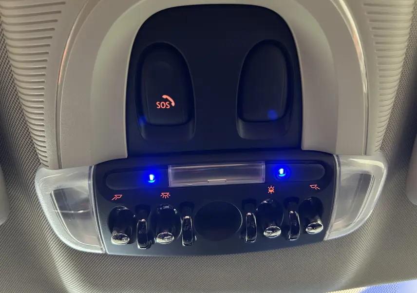 Vue en gros plan du panneau de commandes intérieures avec interrupteurs chromés et boutons SOS éclairés en bleu sur MINI Countryman 2021.
