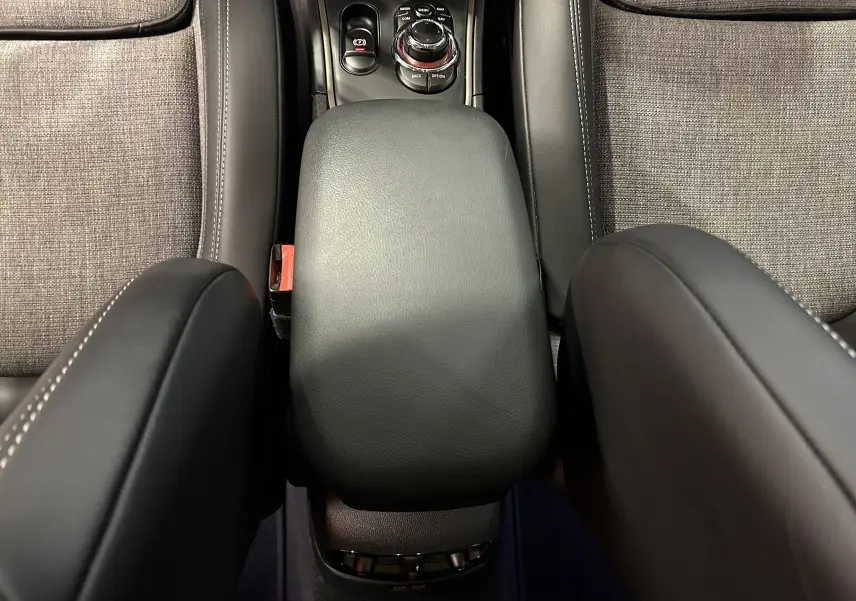 Vue intérieure centrée sur l'accoudoir noir en cuir et la console centrale entre les sièges tissu gris du MINI Countryman.