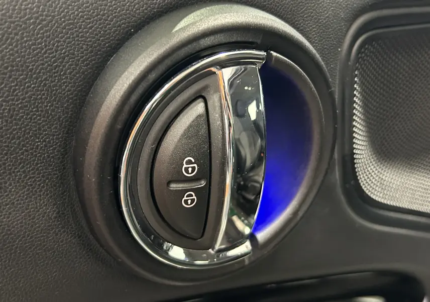Gros plan sur la commande de verrouillage des portes avec éclairage bleu intérieur d'une MINI Countryman vert métallisé.