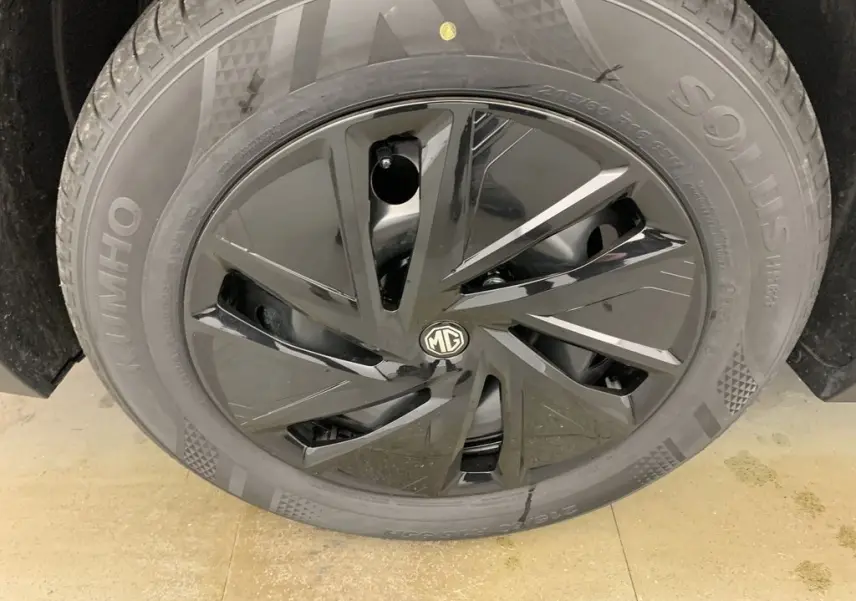 Gros plan sur la jante noire brillante avec logo MG au centre du MG ZS blanc Dover White, roue avant droite visible.