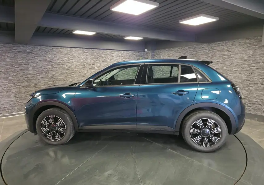 Vue de profil côté gauche d'un FIAT 600 1.2 Hybrid bleu métallisé avec jantes alliage et toit noir en intérieur showroom.
