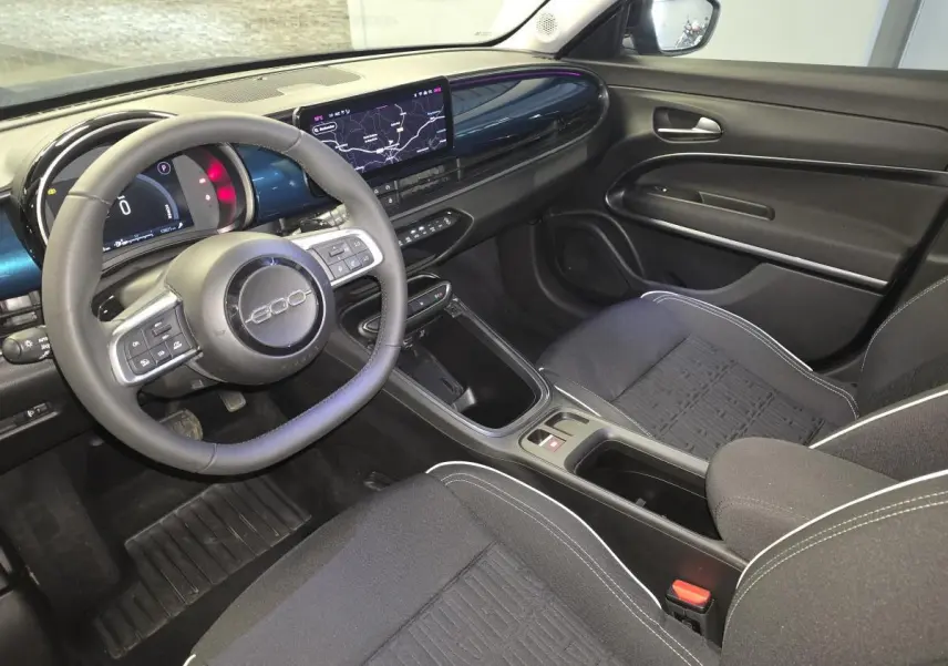 Vue intérieure côté conducteur de la FIAT 600 Hybrid 2025 avec tableau de bord bleu et volant multifonction noir.