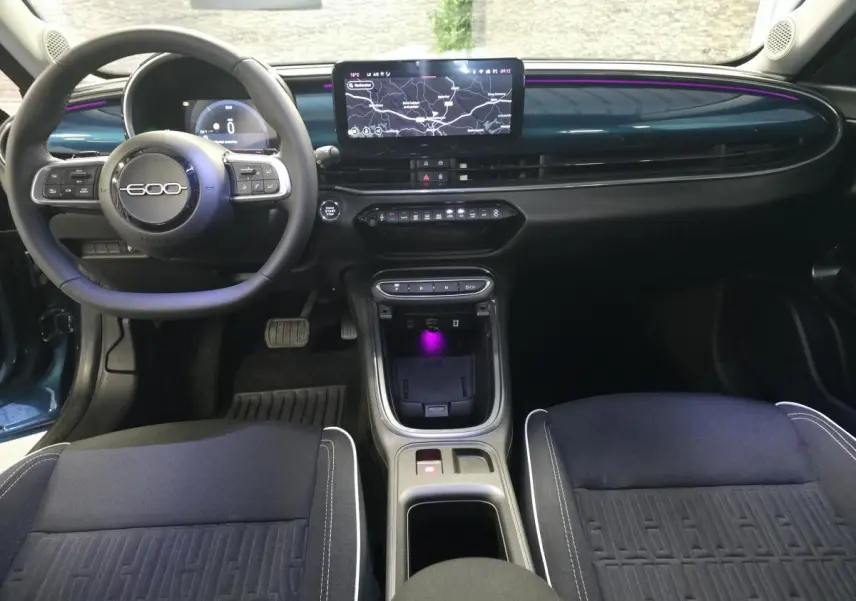 Vue intérieure avant de la Fiat 600 hybride bleue, tableau de bord avec écran central tactile et éclairage d'ambiance violet.