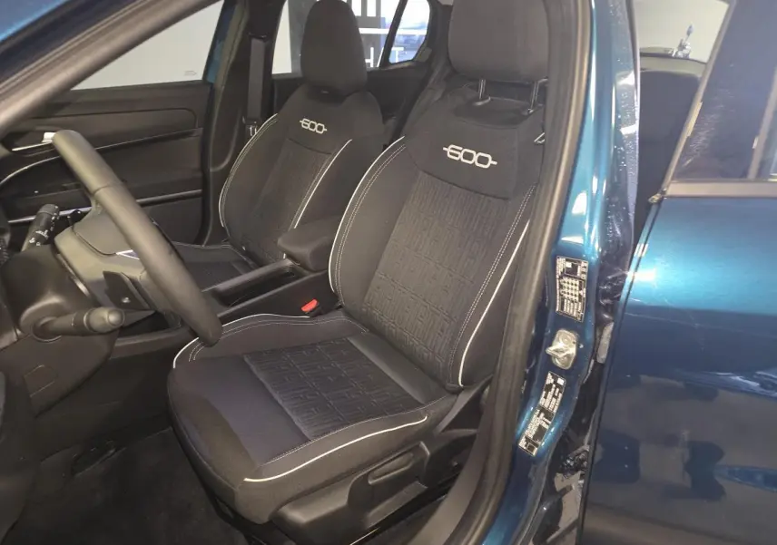 Vue intérieure côté conducteur de la FIAT 600 Hybrid 2025 bleu, sièges noirs avec logo "600" brodé et surpiqûres blanches.
