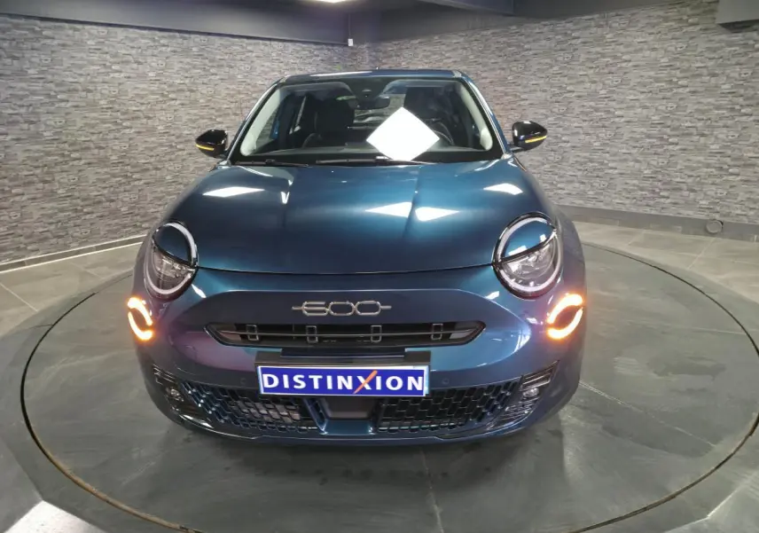 Vue frontale d'une FIAT 600 hybride bleu métallisé avec feux de jour LED allumés en intérieur showroom.