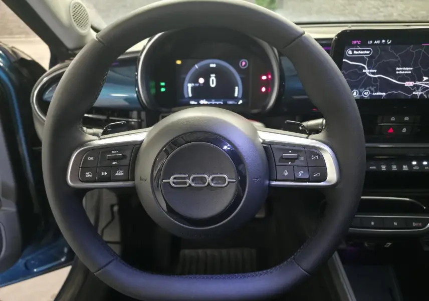 Vue intérieure centrée sur le volant noir de la Fiat 600 1.2 Hybrid 2025 avec tableau de bord numérique et écran tactile.