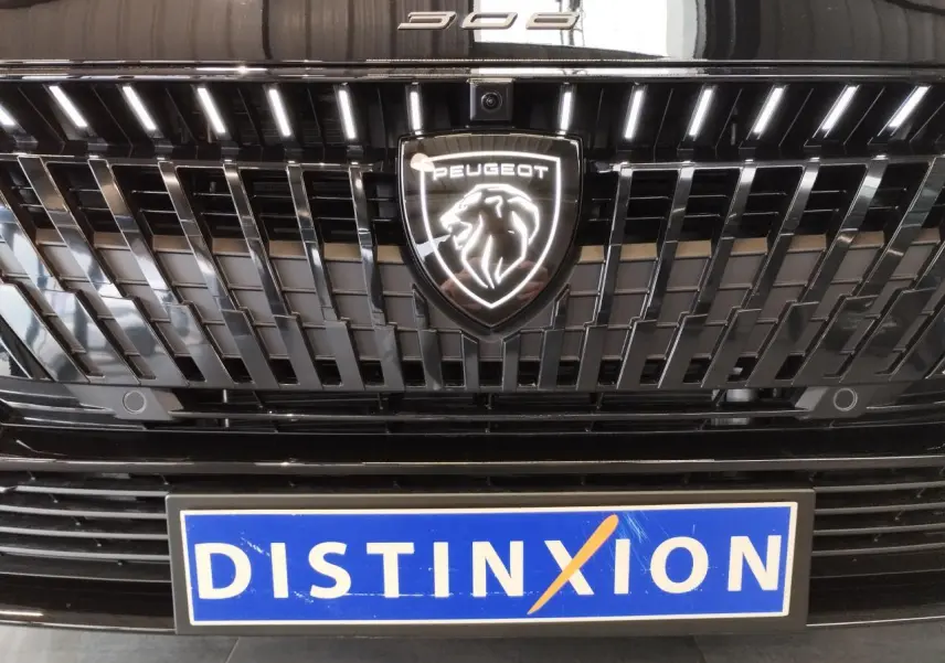 Gros plan sur la calandre noire métallisée de la Peugeot 308 avec logo lion lumineux et plaque Distinxion.