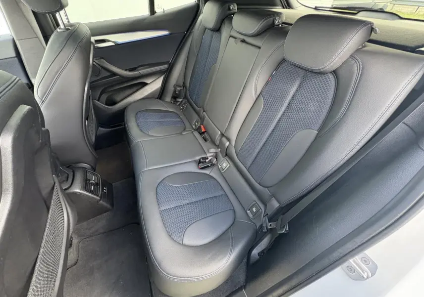 Vue intérieure arrière du BMW X2 blanc alpin, sièges arrière en tissu et similicuir noir avec inserts bleus.