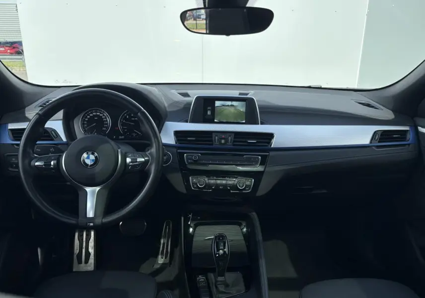 Intérieur BMW X2 vue de face, tableau de bord noir avec écran central et volant M Sport cuir.