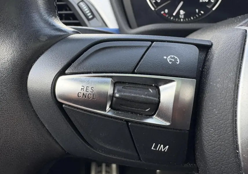 Gros plan sur les commandes de régulateur de vitesse au volant d'une BMW X2 blanche Alpine, finition M Sport.