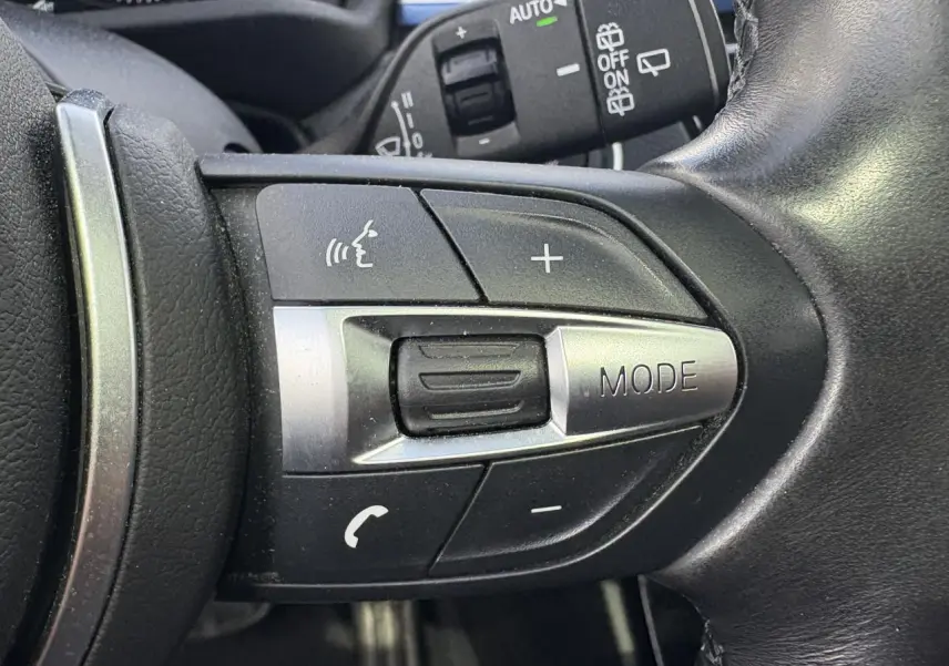 Gros plan sur les commandes multifonctions du volant cuir noir du BMW X2 blanc Alpin, avec bouton mode et volume.