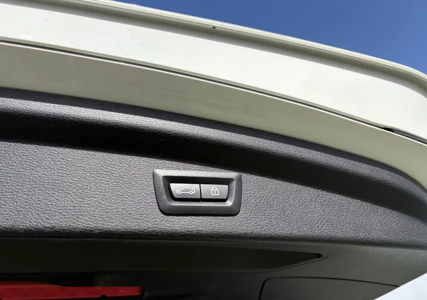 Bouton de commande électrique du hayon sur la partie intérieure du coffre d'un BMW X2 blanc alpin, ciel bleu en arrière-plan