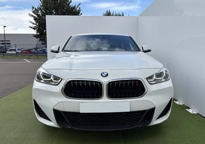 Vue frontale d'une BMW X2 blanche Alpine avec calandre noire et phares LED allumés.