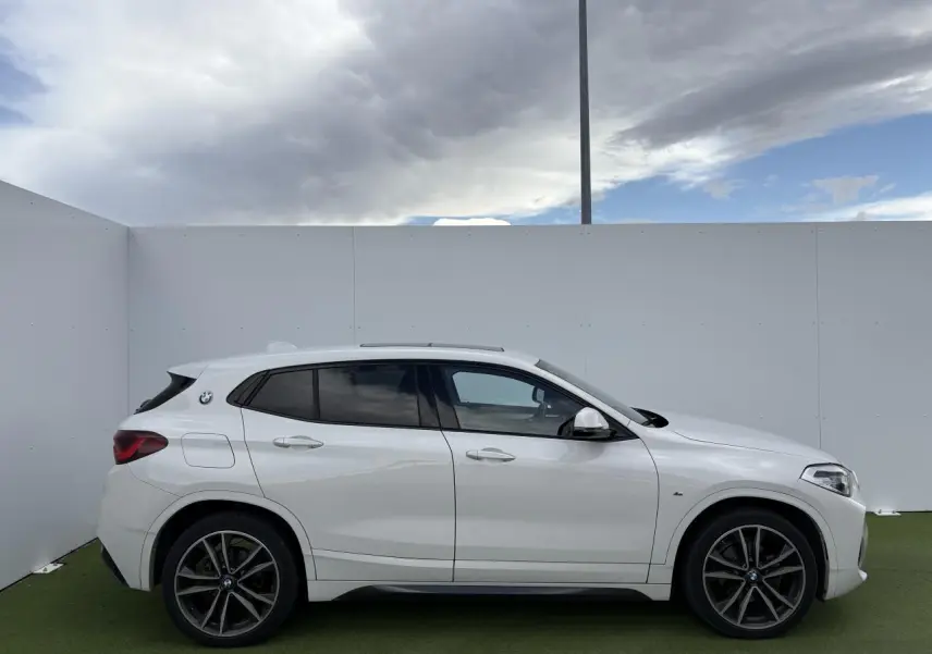 Profil côté gauche d'un BMW X2 blanc alpin avec jantes 19 pouces et toit ouvrant panoramique en verre.