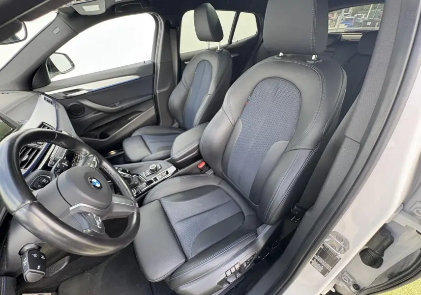 Vue intérieure côté conducteur du BMW X2 blanc avec sièges sport en tissu et similicuir noir et bleu.