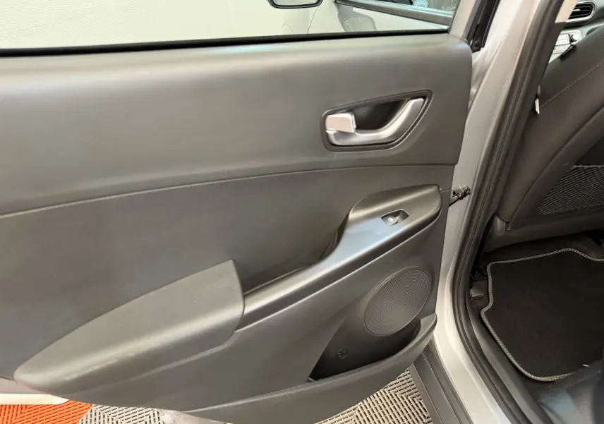 Porte arrière droite ouverte du Hyundai Kona gris clair, montrant la garniture intérieure noire avec poignée et commande de vitre.