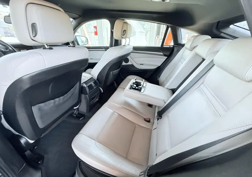 Vue intérieure arrière droite du BMW X6 2011, sièges cuir beige avec accoudoir central déployé et ceintures noires.