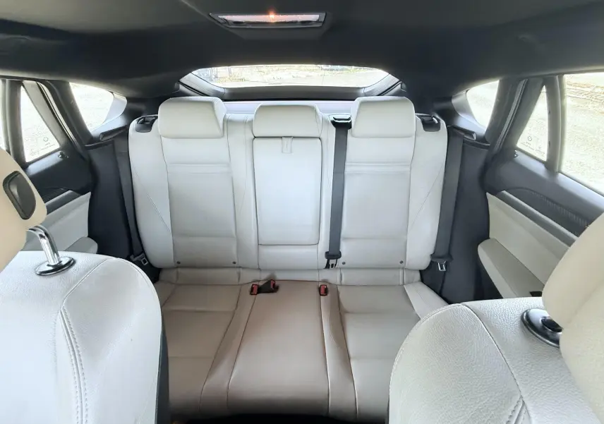 Vue arrière intérieure montrant les sièges arrière en cuir clair du BMW X6 noir de 2011, avec toit ouvrant panoramique.