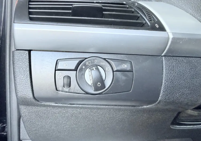 Gros plan sur le panneau de commande des phares intérieur noir du BMW X6 noir, avec molette de réglage et ventilation.