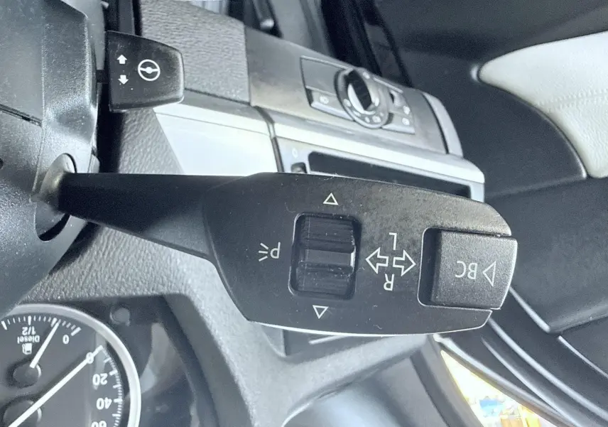 Gros plan sur la commande de clignotant et régulateur de vitesse dans l’habitacle noir d’une BMW X6 noire, vue côté gauche.