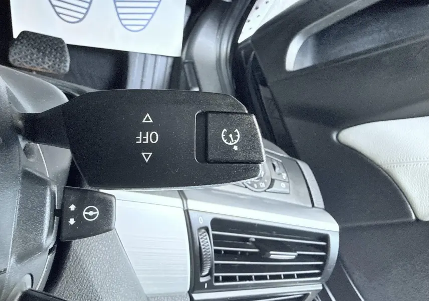 Gros plan sur la commande de régulateur de vitesse dans l’habitacle noir et gris d’une BMW X6 noire, côté gauche du volant.