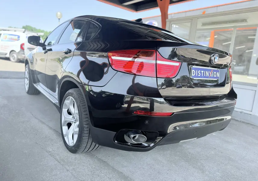 BMW X6 noire vue en 3/4 arrière droit, mettant en valeur ses feux rouges et sa sortie d’échappement chromée.
