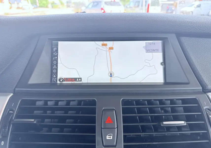 Vue rapprochée de l’écran de navigation central et des aérateurs noirs du tableau de bord d’une BMW X6 noire.
