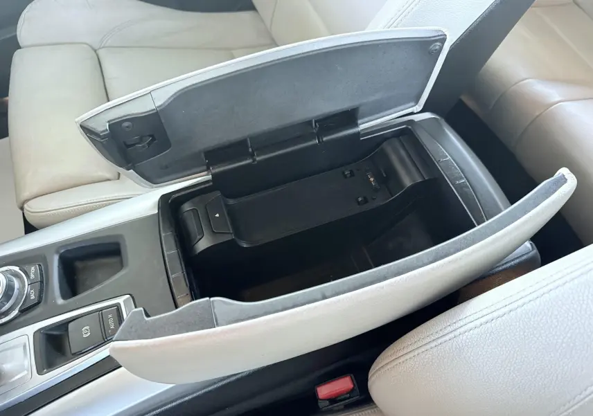 Vue rapprochée de la console centrale ouverte avec rangement, sièges cuir beige clair d’une BMW X6 noire.