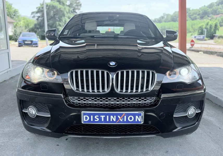 Vue frontale d’un BMW X6 noir avec phares allumés et calandre chromée sous un abri extérieur.