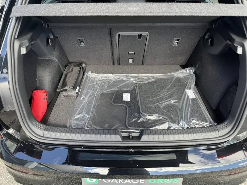 Vue plongeante sur le coffre ouvert d’une Volkswagen Golf noir Grenadilla avec tapis neufs et trousse de secours rouge.