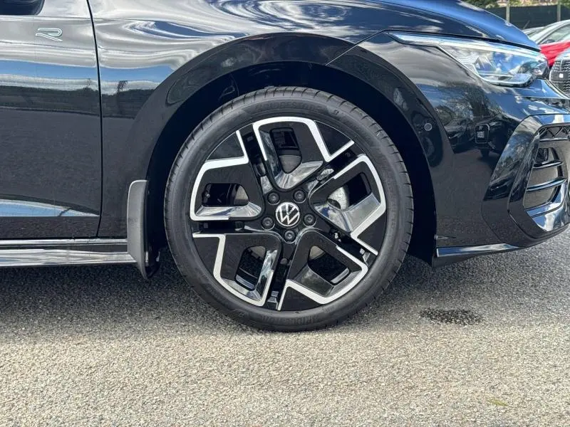 Gros plan sur la roue avant droite noire et jante alu bicolore d'une Volkswagen Golf 1.5 eTSI R-Line Edition noire métallisée.