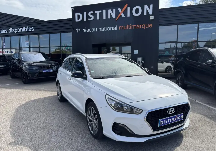 Hyundai i30 SW blanche vue 3/4 avant droit devant un showroom Distinxion avec jantes alliage 17 pouces.