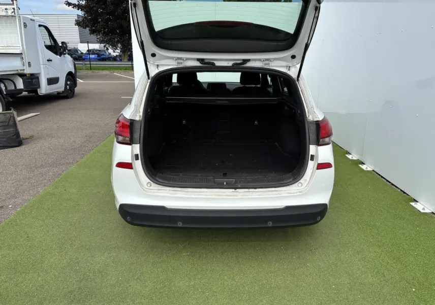 Vue arrière d'un break Hyundai i30 blanc avec coffre ouvert montrant un espace de chargement vide.
