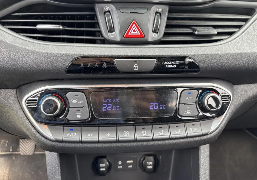Gros plan sur la console centrale de la Hyundai i30 blanche, affichant la climatisation automatique bi-zone et les commandes tactiles.