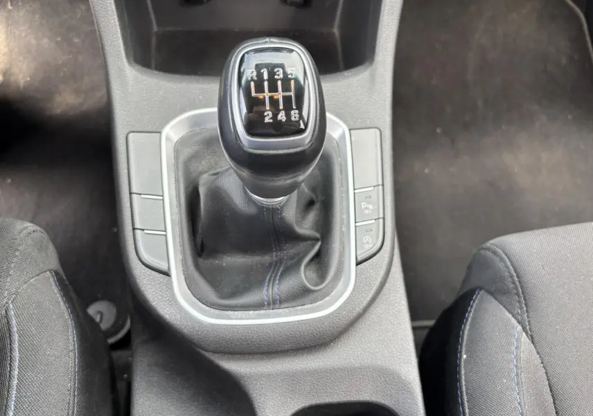 Gros plan sur le levier de vitesses manuel noir avec surpiqûres bleues, entre les sièges avant noirs de la Hyundai i30 blanche.