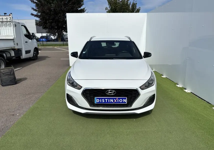 Vue frontale d'une Hyundai i30 SW blanche avec calandre noire et plaques Distinxion sur un sol vert.