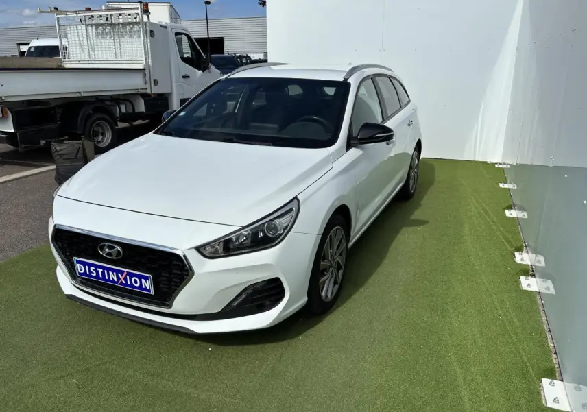 Hyundai i30 SW blanche vue en 3/4 avant droit, avec calandre noire et jantes alliage 17 pouces.