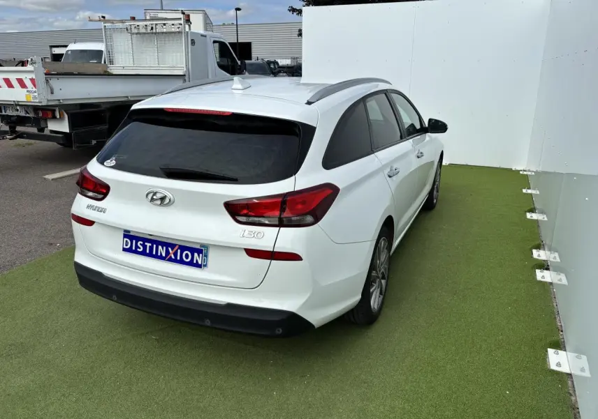 Vue 3/4 arrière droite d'une Hyundai i30 SW blanche avec vitres arrière surteintées et jantes alliage 17 pouces.