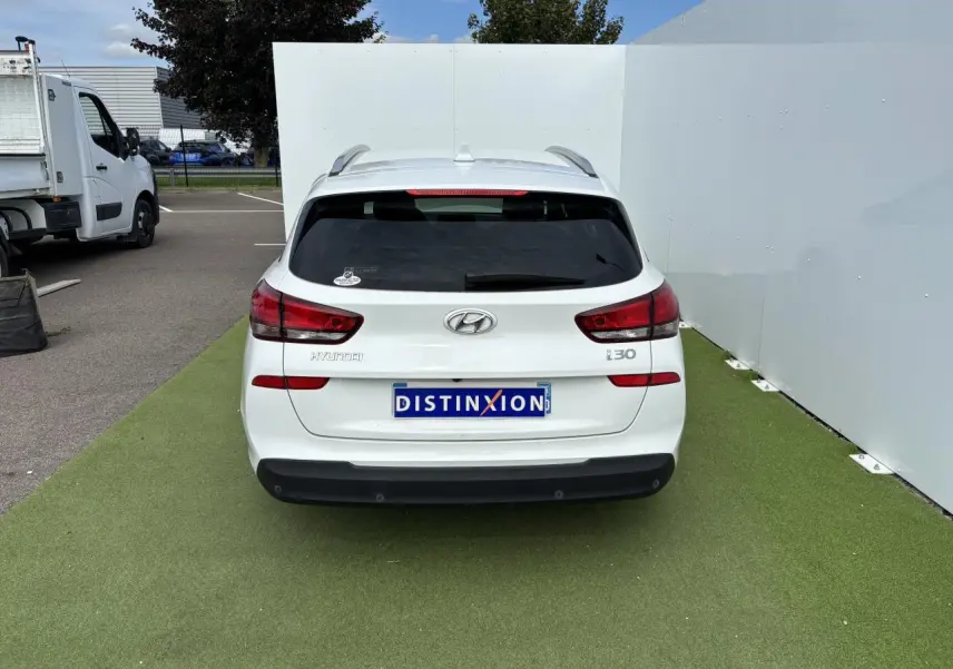 Vue arrière d'une Hyundai i30 blanche stationnée sur sol vert avec logo et feux arrière visibles.