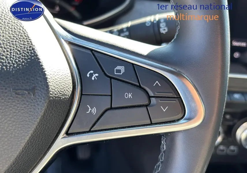 Gros plan sur les commandes multifonctions gauche du volant textile enduit gris de la Renault Clio V 2024.