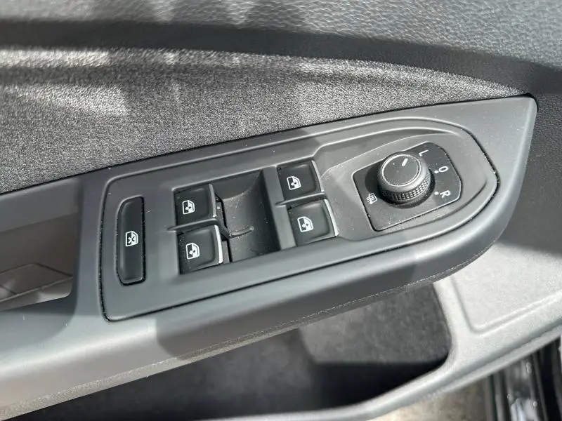 Gros plan sur les commandes de lève-vitres et réglage des rétroviseurs côté conducteur d'une Volkswagen Golf noire nacrée 2024.