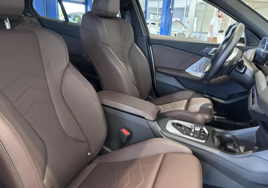Vue intérieure côté conducteur de la BMW Série 1 120d M Sport 2025 avec sièges en cuir marron et console centrale moderne.