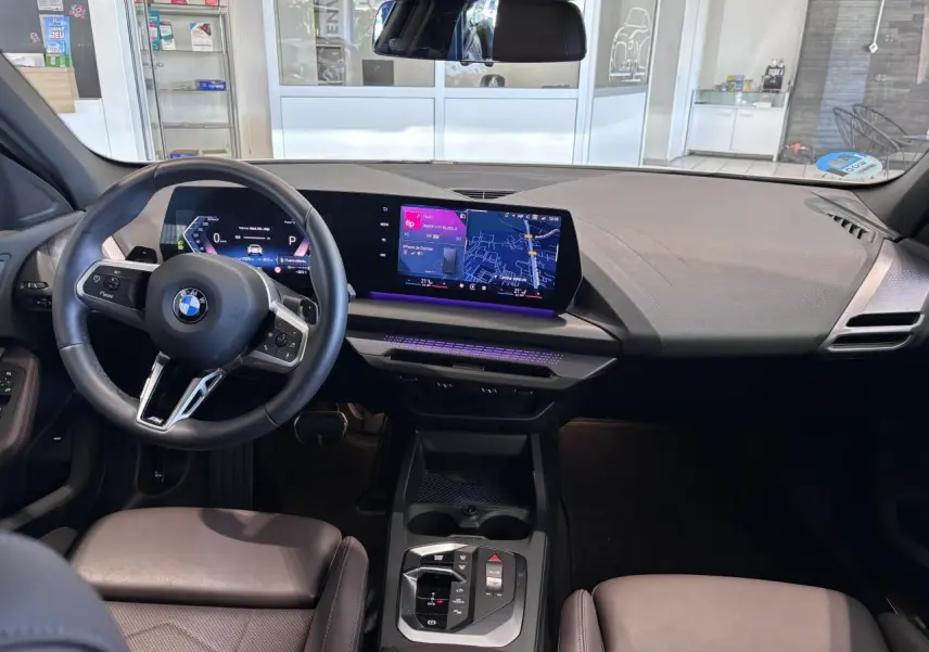 Vue intérieure de la BMW Série 1 120d M Sport 2025, tableau de bord moderne avec écran tactile et éclairage d'ambiance violet.