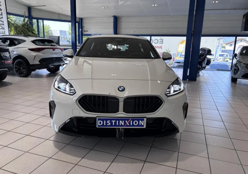 Vue avant d'une BMW Série 1 120d M Sport blanche 2025 en showroom, avec calandre noire et phares allumés.