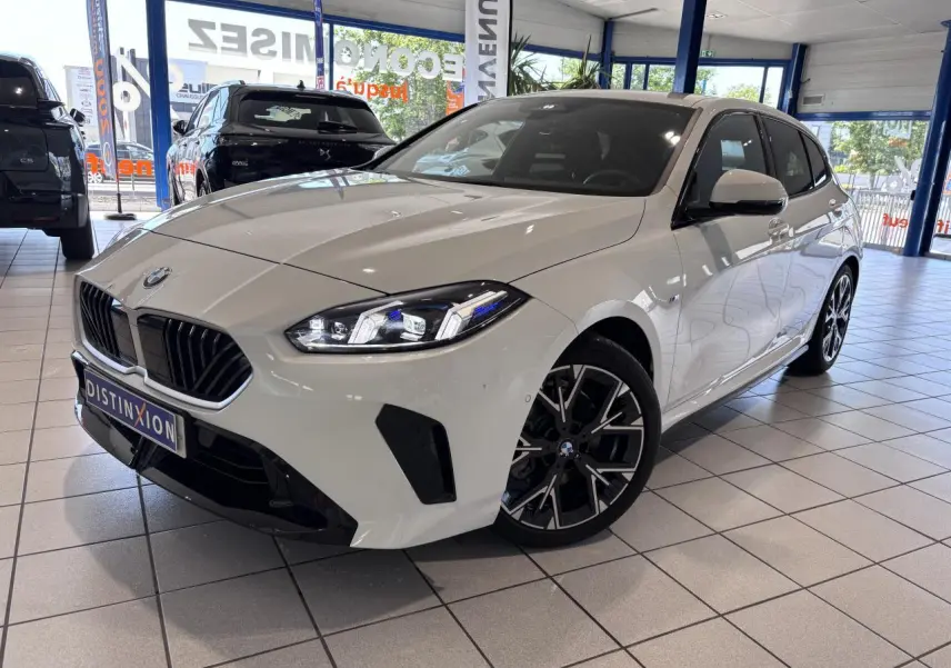 BMW Série 1 120d M Sport blanche vue 3/4 avant droit en showroom, avec jantes noires et calandre noire distinctive.